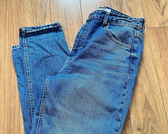Puede incluir: Un par de pantalones vaqueros azules de mezclilla con cintura alta y pierna recta. Los vaqueros tienen un aspecto descolorido y están hechos de una tela suave y cómoda.