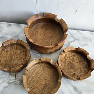 Pode incluir: Conjunto de quatro tigelas de madeira com acabamento marrom escuro. As tigelas são redondas e têm uma borda festonada. As tigelas estão dispostas em forma de pirâmide.