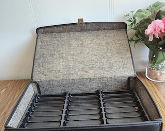 May include: Black leather carrying case with a built-in compartment for storing cassette tapes. The case has a handle and a latch.