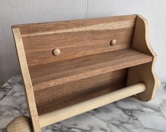 Könnte beinhalten: Ein wandmontierter Papierhandtuchhalter aus Holz mit einem Regal. Der Halter hat eine natürliche Holzoptik und ein schlichtes Design. Er verfügt über eine Holzstange zum Aufhängen einer Papierhandtuchrolle und ein kleines Regal zum Verstauen von Gegenständen.
