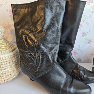 Peut inclure: Une paire de bottes noires mi-mollet avec un bout arrondi lisse et une tige en cuir texturé et froissé. L'extérieur des bottes présente un motif décoratif en forme de feuille cousu sur le côté, avec un talon subtil et une silhouette épurée.