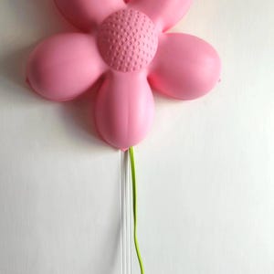 May include: A pink plastic flower-shaped night light with a green cord. The light has a textured center and five petals.