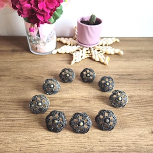 Peut inclure: Dix tirettes de tiroir en métal noir ornées d'un centre doré. Les tirettes sont en forme de fleurs avec des motifs complexes.