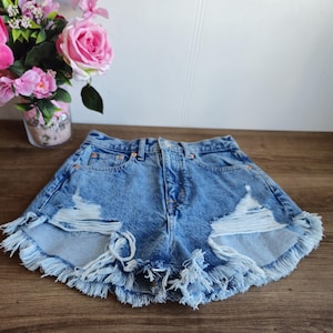 Peut inclure: Short en jean bleu clair avec des bords effilochés et des détails usés. Le short a une taille haute et une coupe décontractée.