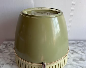 Puede incluir: Secador de pelo vintage verde aguacate y crema. El secador de pelo tiene una forma redondeada y cónica con una base crema con ranuras verticales. Un cierre plateado asegura la base. La parte superior es un tono de verde más claro.