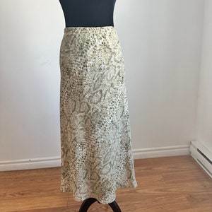 Peut inclure: Une longue jupe fluide à imprimé serpent dans les tons de vert et de blanc. La jupe a une taille ajustée et une silhouette évasée en forme de A.