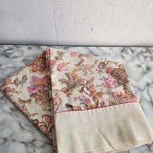 May include: A pair of cream-coloured pillowcases with a floral pattern in shades of pink, orange, and brown. The pillowcases have a pink trim.