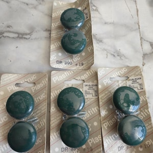 Pode incluir: Quatro pacotes de botões de armário de plástico verde com parafusos prateados. Cada pacote contém dois botões e tem o texto "Plastitruc" e "DP 390 #19" impresso nele.