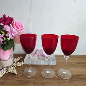 Peut inclure: Trois verres à vin rouge avec des tiges et des bases claires. Les verres sont disposés en rangée sur une surface en bois.