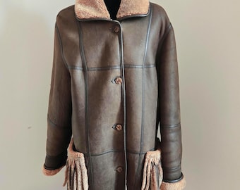 May include: A brown shearling coat with a brown faux fur collar and fringe detailing on the pockets.