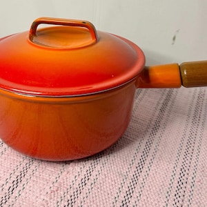Pode incluir: Caçarola de ferro fundido esmaltado laranja com cabo de madeira e tampa.