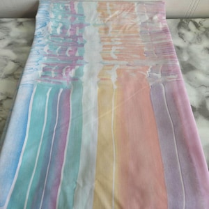 Peut inclure: Un tissu blanc avec un motif de rayures arc-en-ciel. Les rayures sont bleu clair, violet, vert, jaune, orange et rose.