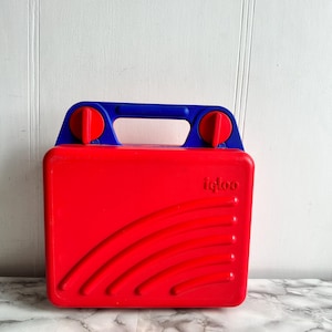 Puede incluir: Fiambrera de plástico roja y azul con asa y cierres. La fiambrera tiene la palabra "igloo" impresa en la parte delantera.