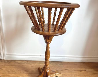 May include: A wooden plant stand with a round top and a spindle design. The stand has a four-legged base.