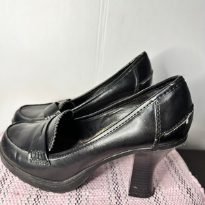 May include: Black leather heeled shoes with a chunky heel and a pointed toe.