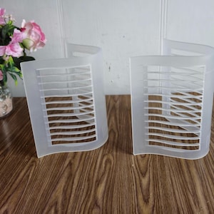 May include: Two white plastic CD storage racks with a curved design and a grid pattern. The racks are empty and sitting on a wooden surface.