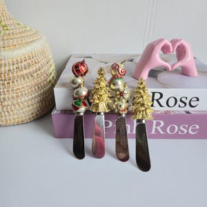 Peut inclure: Ensemble de quatre couteaux à beurre décoratifs de Noël. Chaque couteau présente une lame en acier inoxydable et un manche festif avec des ornements ou un motif de sapin de Noël doré. Les manches ont des accents rouges, argentés et dorés.