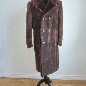 May include: A long brown suede coat with a faux fur collar and double breasted closure. The coat has silver buttons and is on a black mannequin.