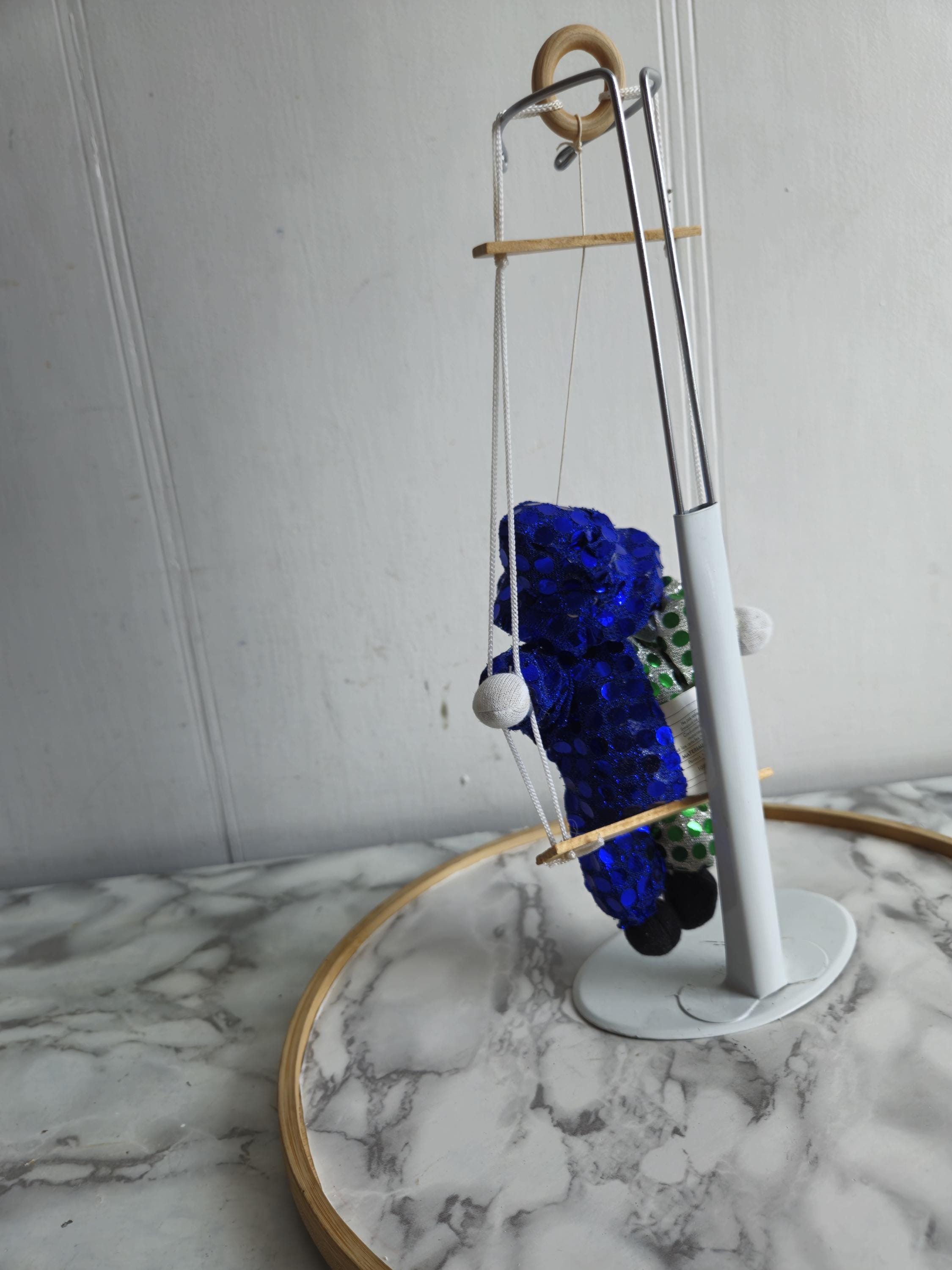 ブランコに乗ったヴィンテージの磁器製ピエロ人形。緑と青の布が
