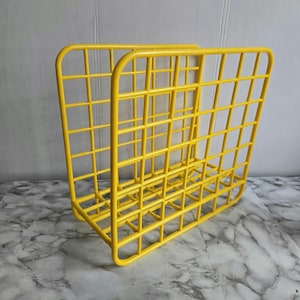 May include: A bright yellow metal magazine rack with a grid design. The rack is made of wire and has a rectangular shape.