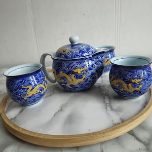 Op de afbeelding: Een blauwe en gouden theeset met een theepot en twee kopjes. De theepot en kopjes zijn versierd met een drakenontwerp.