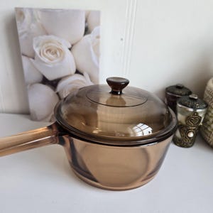 Puede incluir: Una taza de cerámica blanca con un asa negra y el texto "But First, Coffee" en negro, con una fuente de estilo manuscrito. La taza está sobre una superficie blanca.