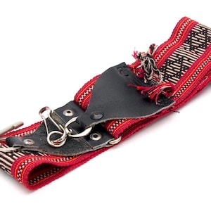 May include: A red and black camera strap with a leather detail and metal clasps. The strap is woven with a geometric pattern.