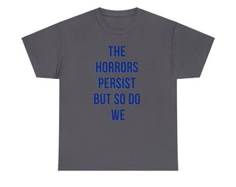 May include: A dark gray t-shirt with the text "THE HORRORS PERSIST BUT SO DO WE" printed in blue.