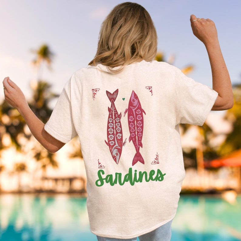 Distressed oversized graphic tee with a vintage fisherman aesthetic. Small red sardines graphic on the front chest, full-size distressed red sardines print on the back with sardines in green script. Nautical, retro inspired design with a worn-in look