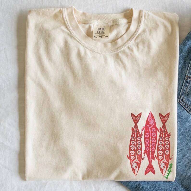 Distressed oversized graphic tee with a vintage fisherman aesthetic. Small red sardines graphic on the front chest, full-size distressed red sardines print on the back with sardines in green script. Nautical, retro inspired design with a worn-in look
