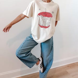 Hand drawn TEACH apple shirt for teachers on ivory tee, vintage childlike apple sketch with imperfect pencil lines and red crayon texture, Free People inspired teacher style
