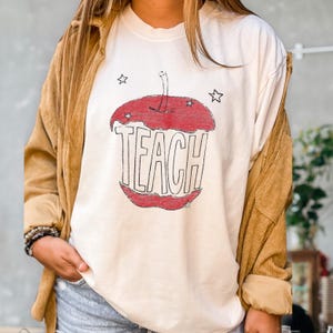 Hand drawn TEACH apple shirt for teachers on ivory tee, vintage childlike apple sketch with imperfect pencil lines and red crayon texture, Free People inspired teacher style