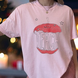 Soft pink teacher t shirt with hand sketched apple core and TEACH text, artsy minimalist teacher shirt with child drawn vintage look
