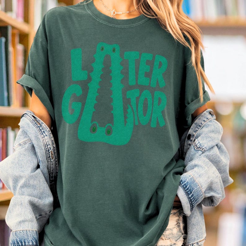 Blue Spruce Comfort Colors graphic tee featuring a playful Later Gator alligator illustration forming the letter A in chunky retro green typography.
