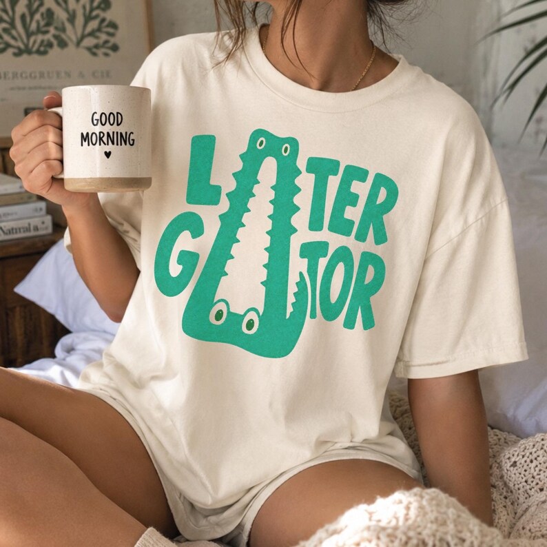 IVORY Comfort Colors graphic tee featuring a playful Later Gator alligator illustration forming the letter A in chunky retro green typography.