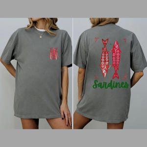 Distressed oversized graphic tee with a vintage fisherman aesthetic. Small red sardines graphic on the front chest, full-size distressed red sardines print on the back with sardines in green script. Nautical, retro inspired design with a worn-in look