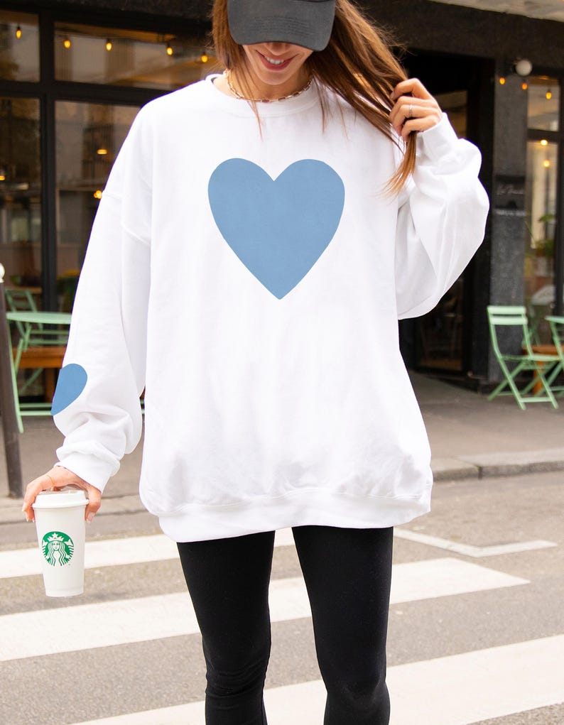 White crewneck sweatshirt featuring a large Carolina blue heart on the chest and a smaller matching Carolina blue heart on the right sleeve.