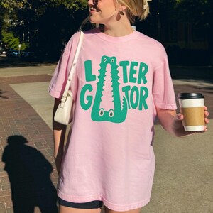 BLOSSOM light pink Comfort Colors  graphic tee featuring a playful Later Gator alligator illustration forming the letter A in chunky retro green typography.