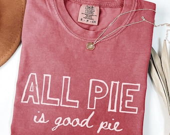 May include: A red t-shirt with the text "ALL PIE is good pie" in white outlined letters. The shirt is made of a soft, comfortable material.