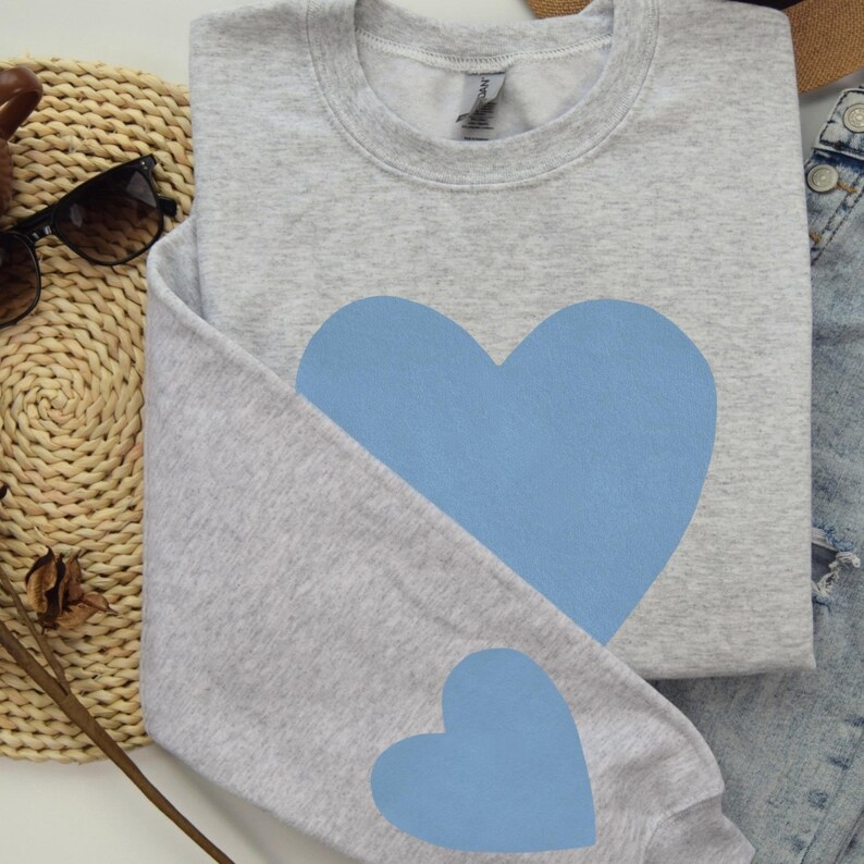 Ash grey crewneck sweatshirt featuring a large Carolina blue heart on the chest and a smaller matching Carolina blue heart on the right sleeve.