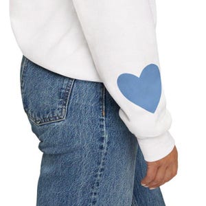 White crewneck sweatshirt featuring a large Carolina blue heart on the chest and a smaller matching Carolina blue heart on the right sleeve.