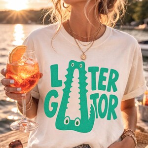 IVORY Comfort Colors happy hour graphic tee featuring a playful Later Gator alligator illustration forming the letter A in chunky retro green typography.