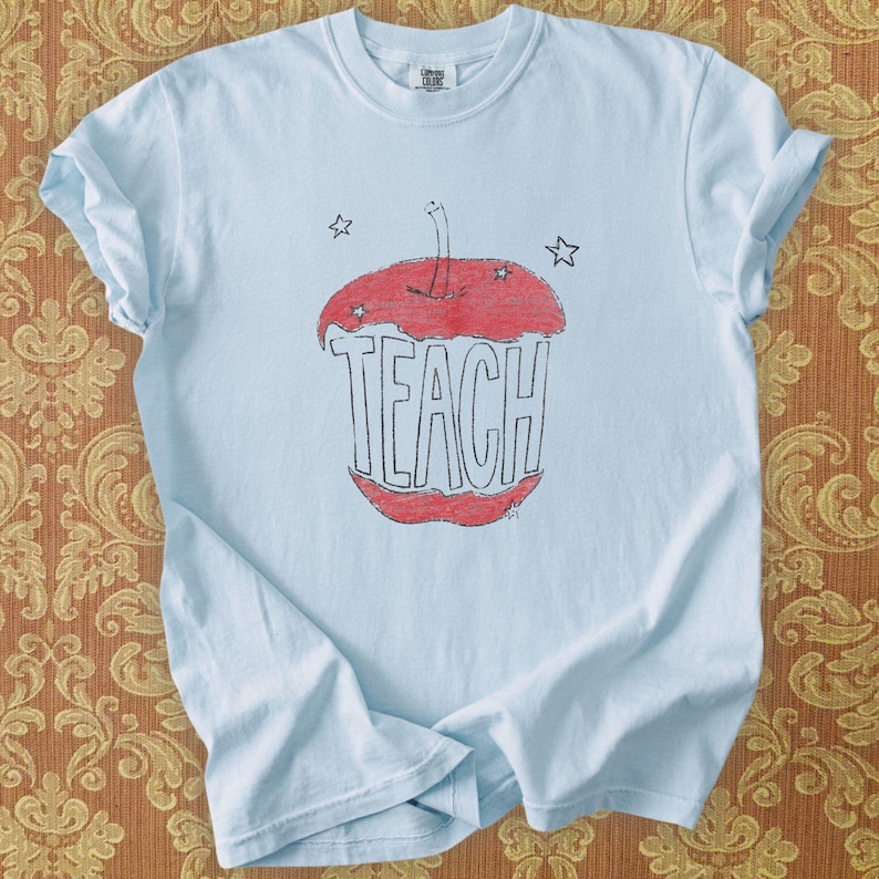 Light blue teacher shirt featuring hand drawn apple illustration and TEACH lettering, relaxed boho teacher tee with Free People inspired aesthetic