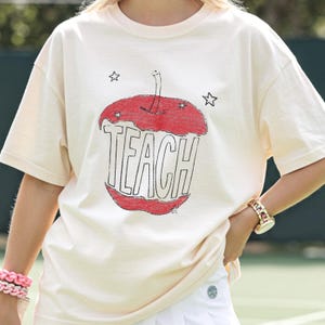 Hand drawn TEACH apple shirt for teachers on ivory tee, vintage childlike apple sketch with imperfect pencil lines and red crayon texture, Free People inspired teacher style