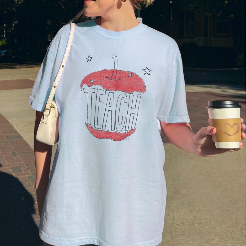 Light blue teacher shirt featuring hand drawn apple illustration and TEACH lettering, relaxed boho teacher tee with Free People inspired aesthetic