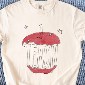 Hand drawn TEACH apple shirt for teachers on ivory tee, vintage childlike apple sketch with imperfect pencil lines and red crayon texture, Free People inspired teacher style