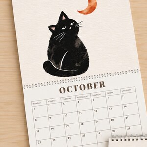 October black cat calendar page with watercolor black cat looking at orange crescent moon, cozy seasonal cat artwork