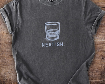 May include: Dark gray t-shirt with a white illustration of a glass of liquor and the text "NEAT ISH." The shirt has a crew neck and short sleeves, with the sleeves rolled up. The shirt is made of a soft, comfortable material.