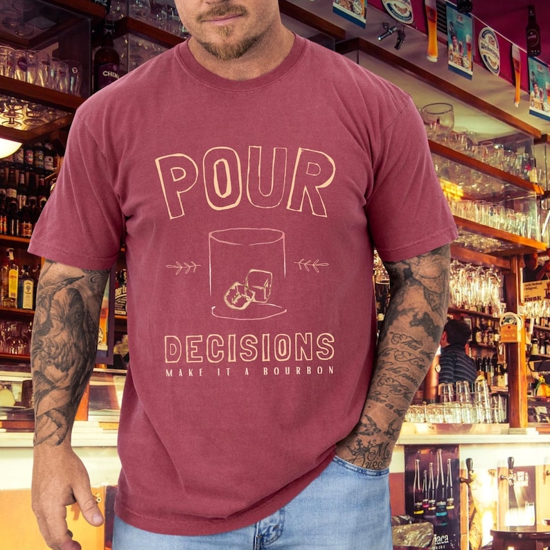 For the bourbon lovers! POUR DECISIONS (make it a bourbon) with a simple distressed line drawing of a whiskey glass with two ice-cubes. Cream graphics on brick COMFORT COLORS.