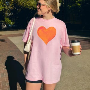 Comfort Colors pink t-shirt with watercolor orange heart design in blossom and crunchberry pink.